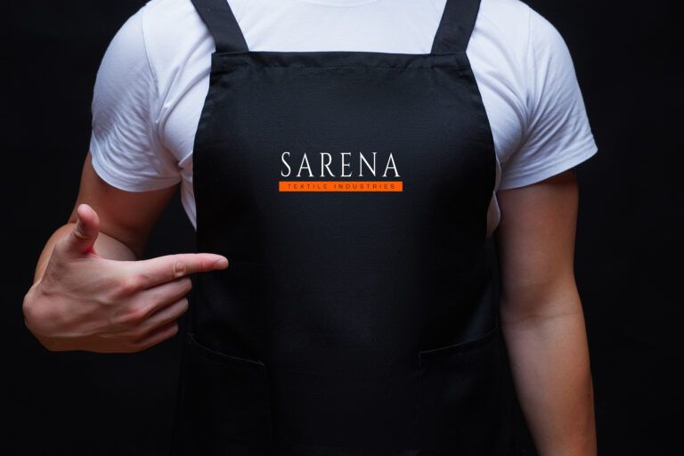 Strong guy torso wearing black apron showing to apron center with his finger. Chef concept mock up or waiter. Dark background