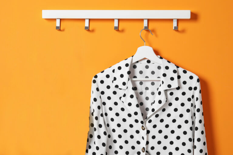 Hanger with polka dot shirt and bag on orange wall